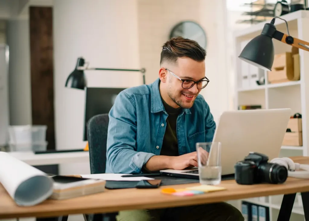 A man sat at a desk in a home office using a laptop