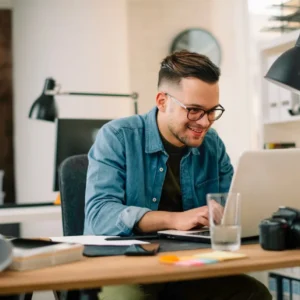 A man sat at a desk in a home office using a laptop