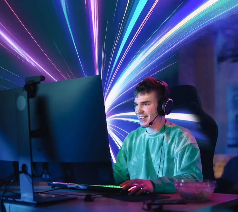 Male gamer sat at a computer desk wearing a headset and gaming on a pc