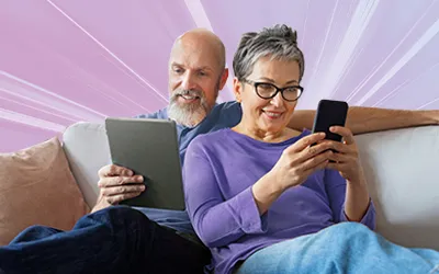 Older couple sat casually on a sofa using a tablet and phone