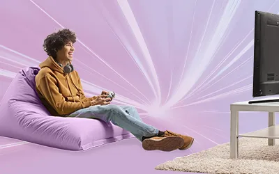 Young adult boy sat on a bean bag holding a game controller looking at a flat screen tv