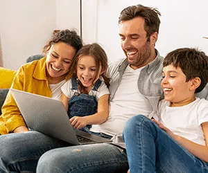 A family of a mum, dad, son and daughter on a sofa together looking at a laptop