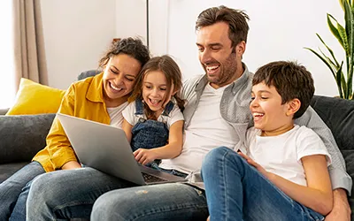 A family of a mum, dad, son and daughter on a sofa together looking at a laptop