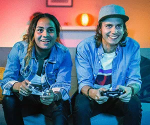 Young adult gamers one male and female holding games controllers immersed in gaming